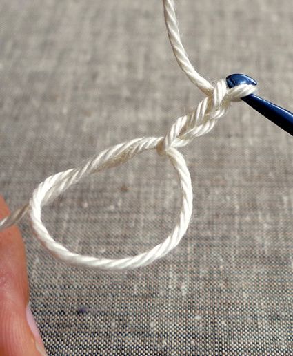 someone crocheting the end of a piece of white yarn with a blue needle