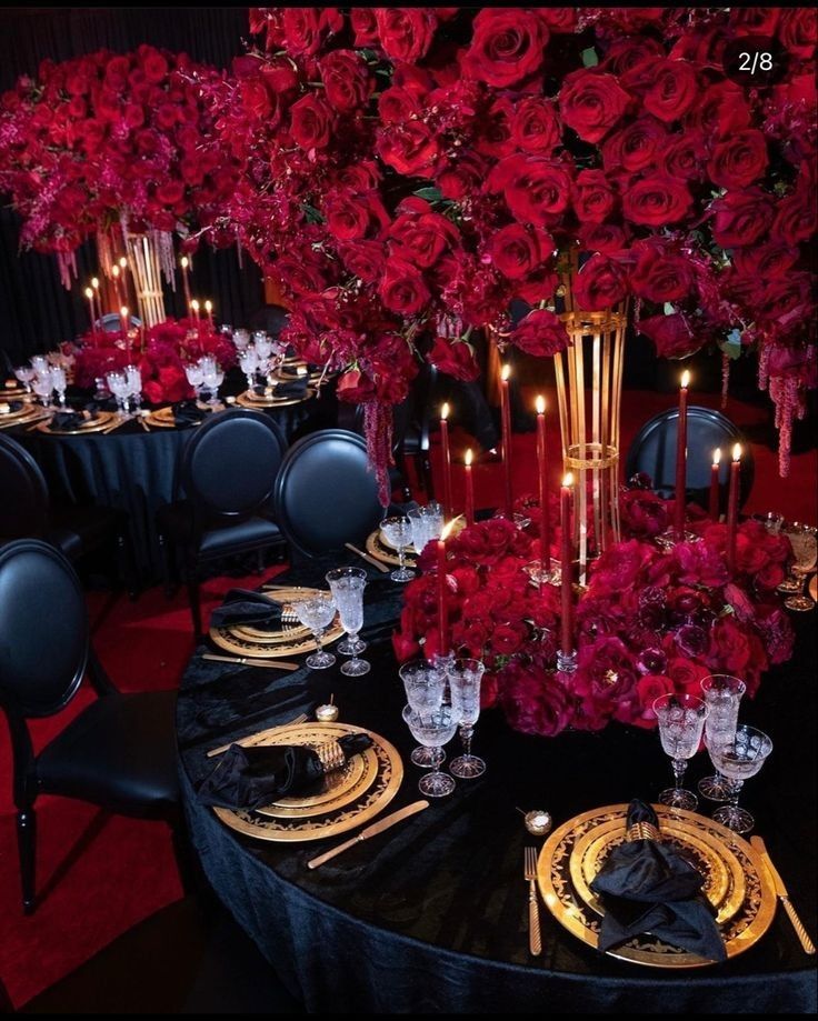 a black table topped with lots of red flowers and place settings next to tall vases filled with roses