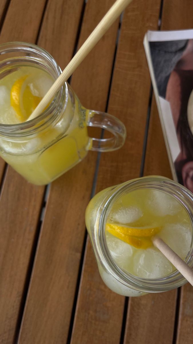 two mason jars filled with lemonade sitting on top of a wooden table next to an open book