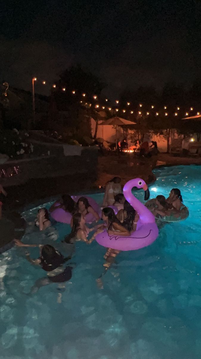 people are in the pool at night with an inflatable flamingo floater