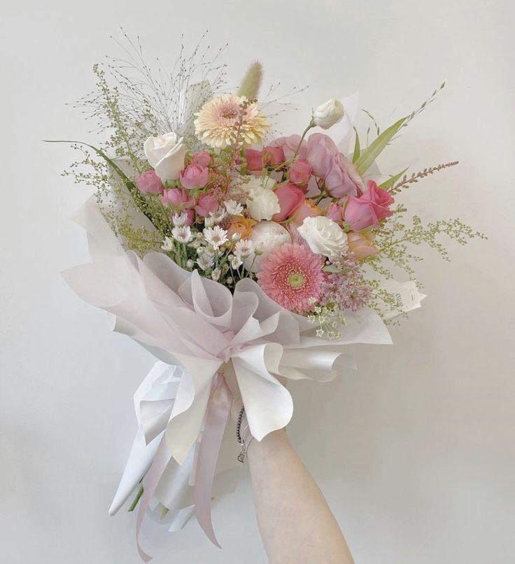 a woman's hand holding a bouquet of pink and white flowers