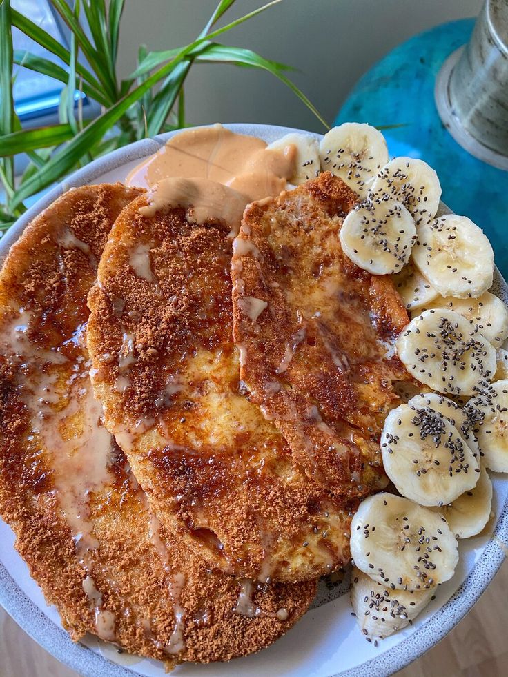 two pancakes with bananas and peanut butter on a plate next to a potted plant