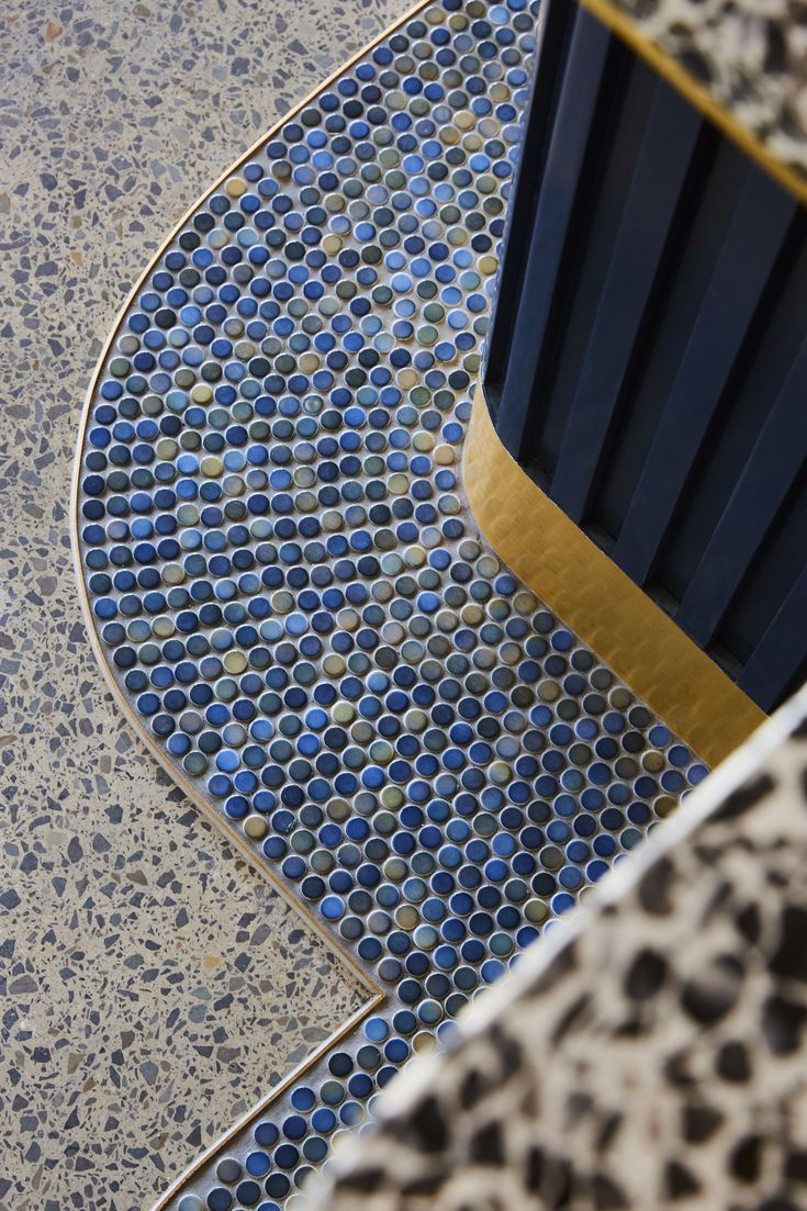 a blue chair sitting on top of a floor next to a tile covered wall with gold trim