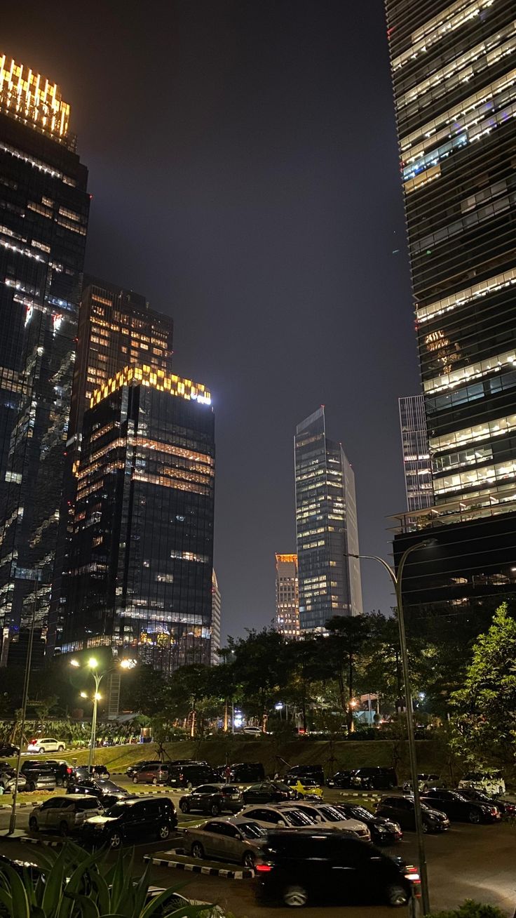 the city is lit up at night with skyscrapers in the background and cars parked on the street