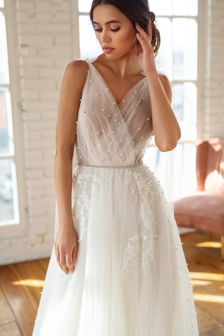 a woman in a white dress is holding her hand up to her ear and looking down