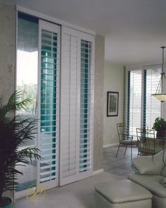 a living room filled with furniture and windows covered in shuttered glass doors next to a dining table