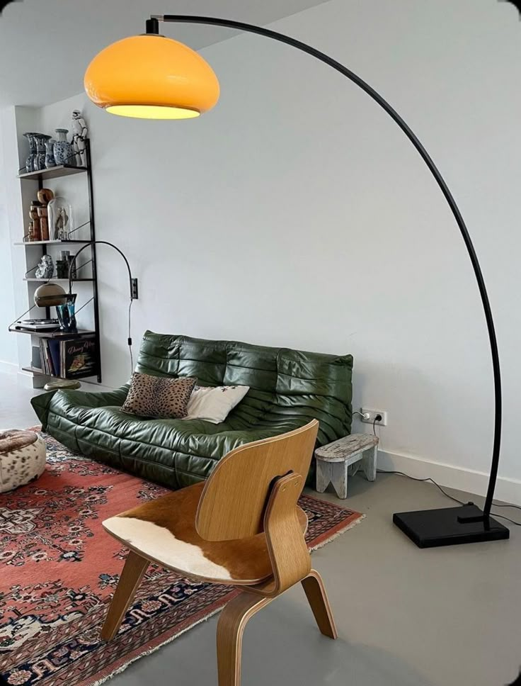 a living room with a green leather couch and an orange lamp on the floor next to it