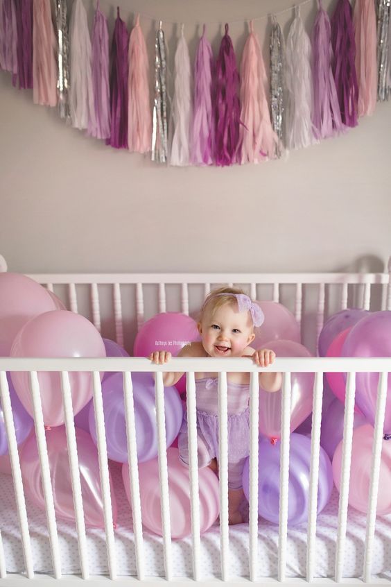 a baby in a crib surrounded by balloons