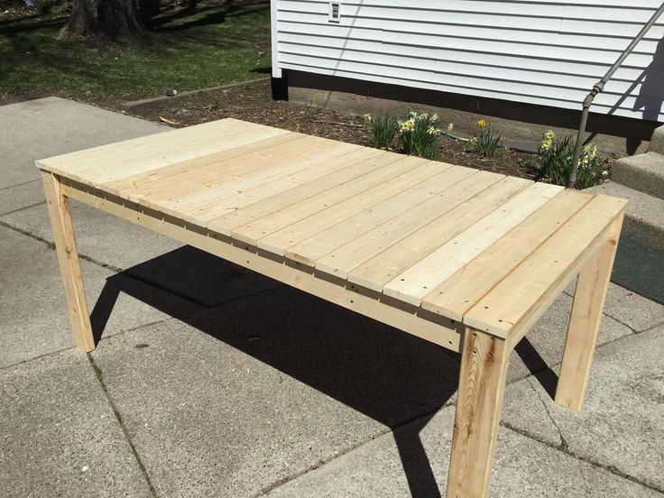 a wooden table sitting on top of a sidewalk next to a white house in the background