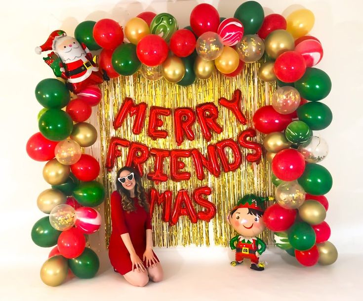 a woman standing in front of a merry friend's christmas photo frame with balloons and streamers