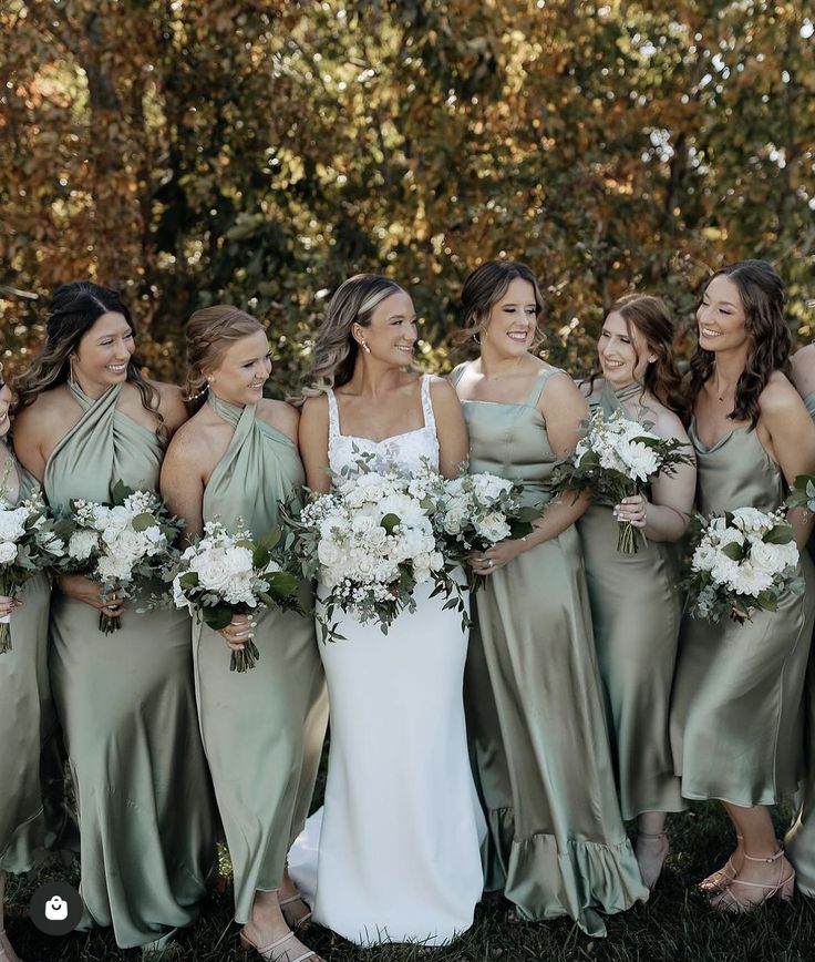 a group of women standing next to each other holding bouquets in front of trees