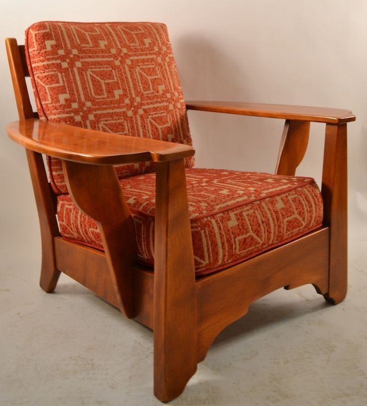 a wooden chair with an orange patterned upholstered back and arm rests against a white wall