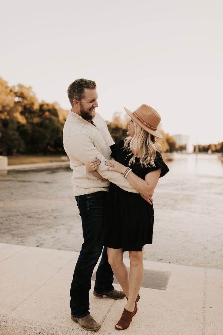 a man and woman standing next to each other in front of a body of water