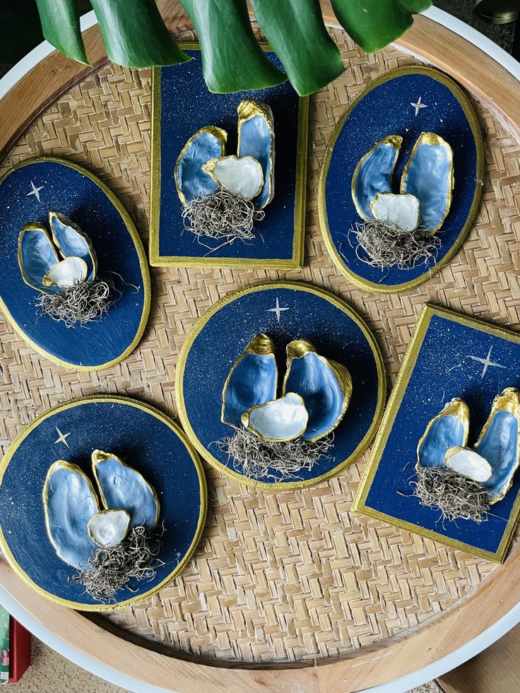 blue and gold plates with shells on them sitting on a wicker tray next to plants