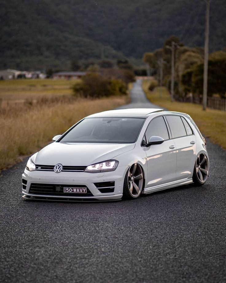 a white car parked on the side of a road next to some grass and trees