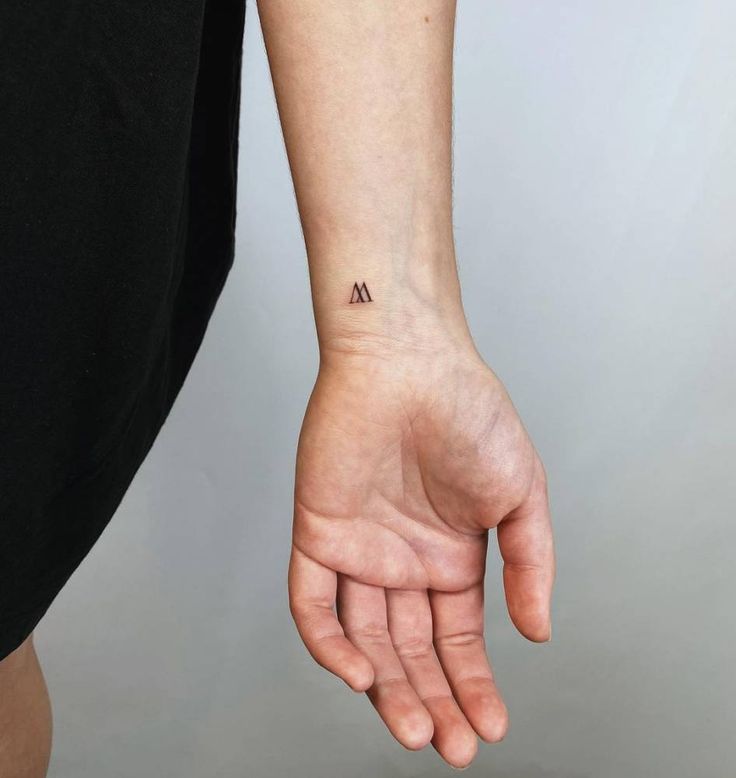 a person with a small tattoo on their left wrist and hand holding the other arm