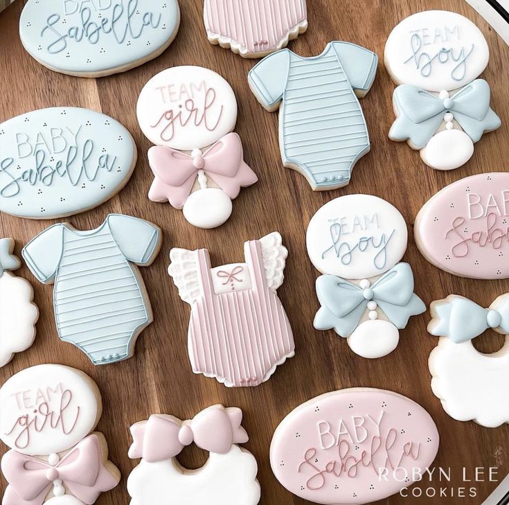 baby shower cookies are arranged on a wooden table with pink and blue onesuits