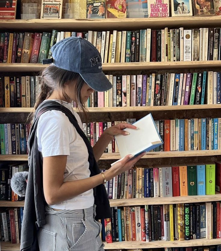 a woman standing in front of a bookshelf holding a book and looking at it