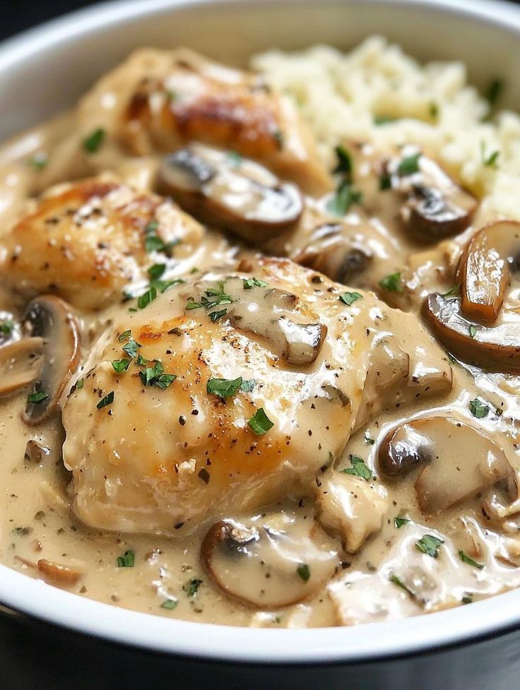 a white bowl filled with chicken and mushrooms covered in gravy next to rice