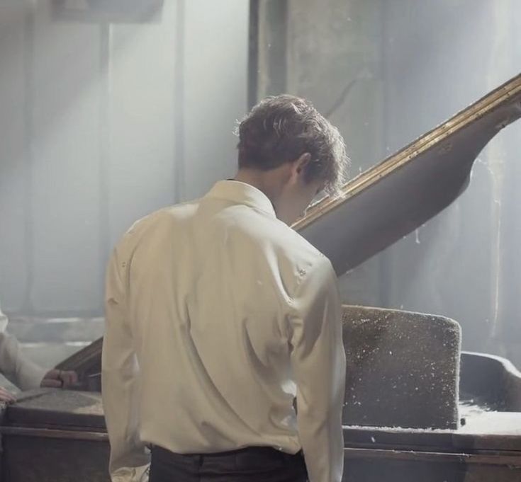 a man standing next to a piano in front of a stained glass window with sunlight streaming through it