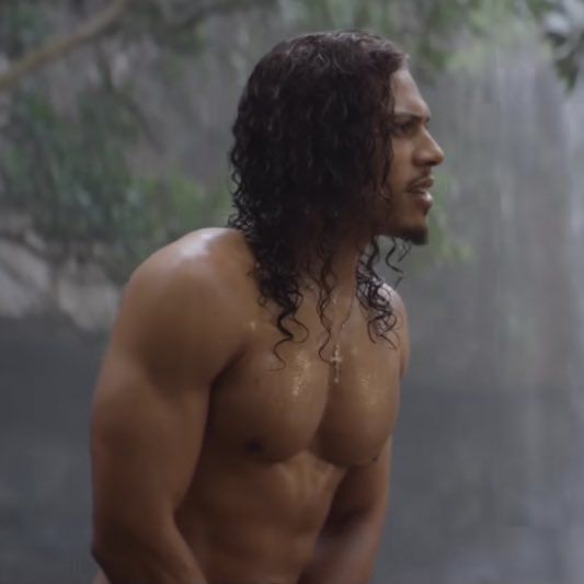 a shirtless man standing in front of a waterfall with his hands on his hips