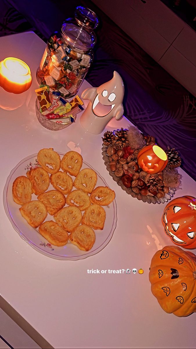 a table topped with lots of cookies next to a lit candle and some pumpkins