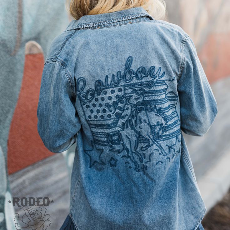 Patriotic Cowboy Button Up by Rodeo Quincy is a cute denim shirt with the design embroidered in blue on the back. Made of denim, it can be dressed up or down for any occasion. With pearl snap buttons, this button up exudes a timeless and sophisticated appeal. True to Size Embroidered Denim Fabric Dark Wash Cotton Tops For Rodeo, Western Style Denim Blue Denim Top, Western Style Medium Wash Cotton Denim Jacket, Western Style Cotton Denim Jacket In Medium Wash, Long Sleeve Cotton Denim Jacket For Rodeo, Dark Wash Relaxed Fit Top For Rodeo, Casual Medium Wash Top For Rodeo, Casual Cotton Denim Jacket For Rodeo, Dark Wash Button-up Tops For Rodeo