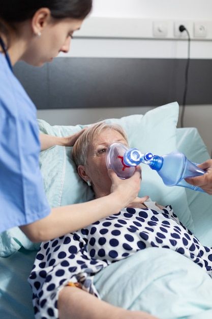 a woman laying in bed with an oxygen tube attached to her mouth and a nurse tending to the patient