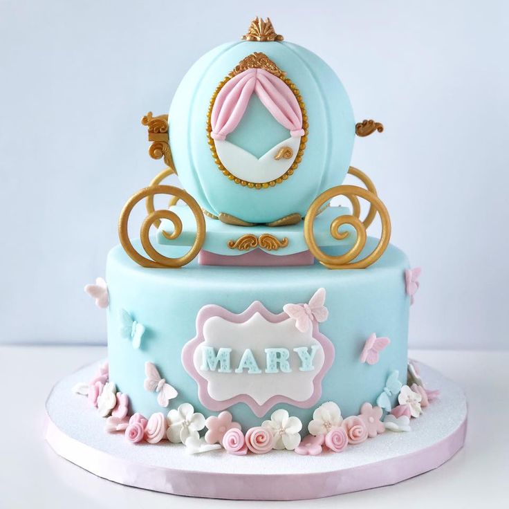 a blue and pink birthday cake with a carriage on the top that says mary in gold