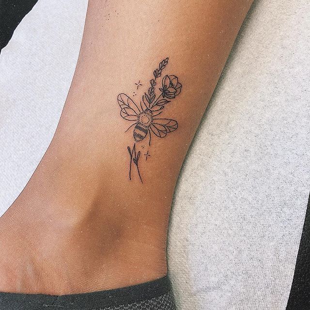 a woman's foot with a flower and bee tattoo on her left side ankle