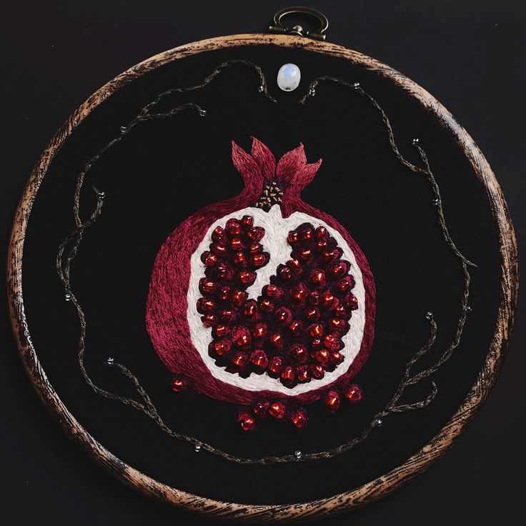 an embroidered pomegranate is displayed on a black surface with red beads around it