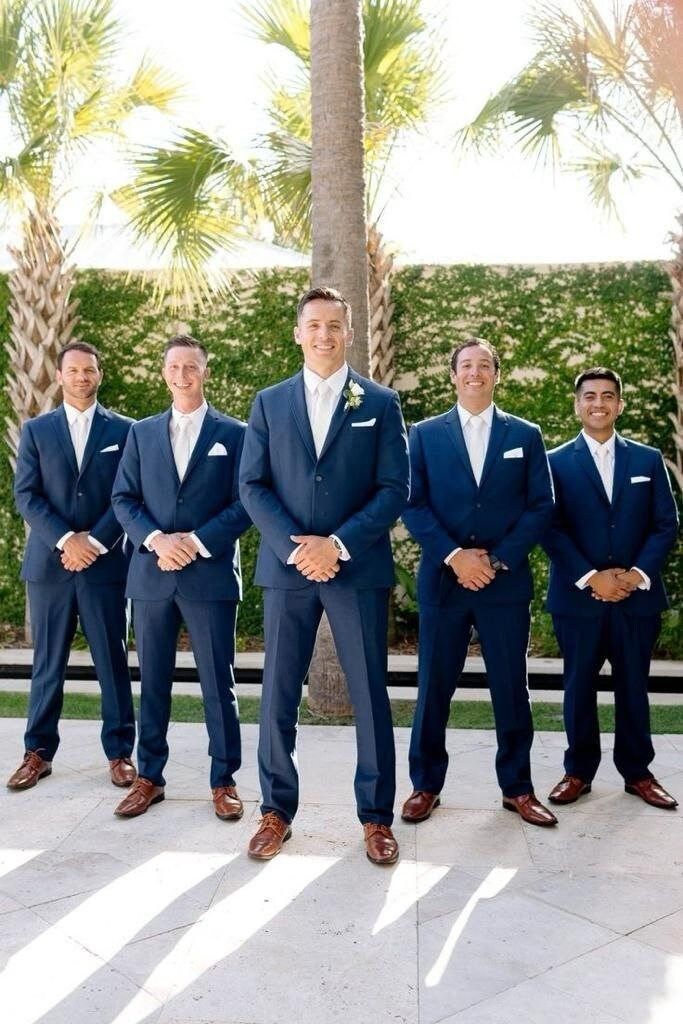 a group of men in suits standing next to each other on a stone floor with palm trees behind them