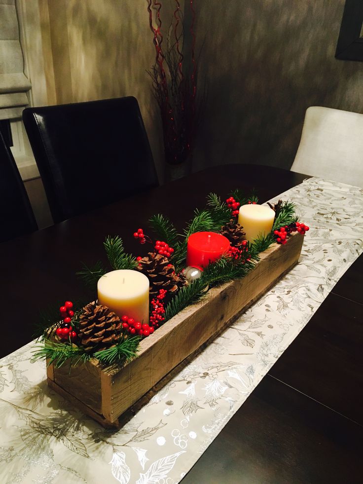 a wooden box with candles and pine cones on it sitting on a dining room table