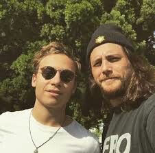 two men standing next to each other with trees in the background