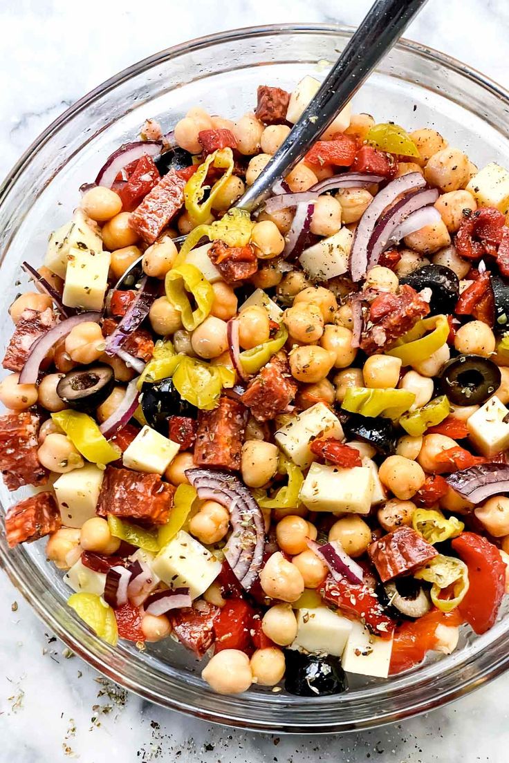 a glass bowl filled with chickpeas, tomatoes, onions and olives next to a spoon