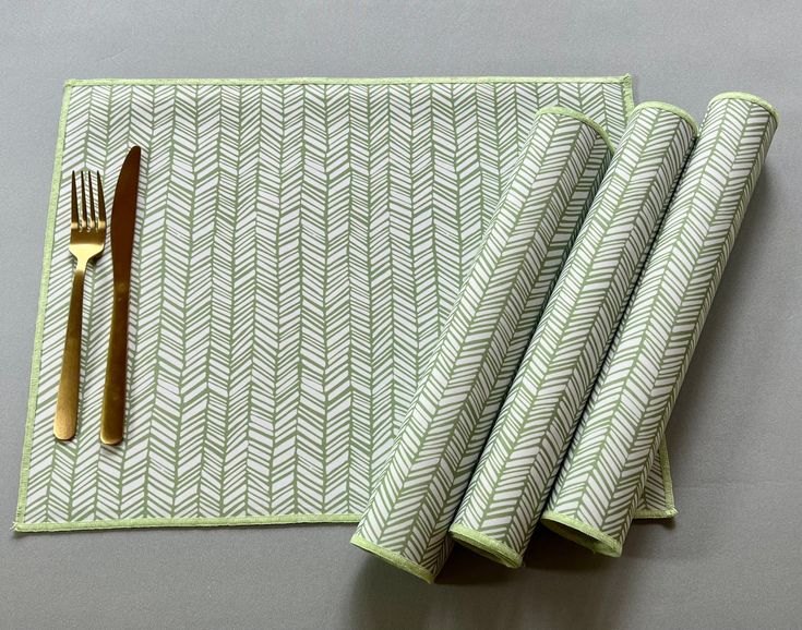 two napkins and a fork on a table with a green place mat next to it