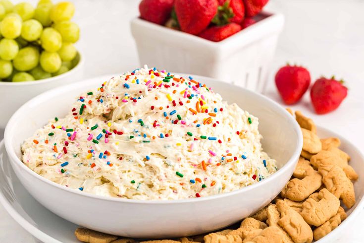 a bowl of ice cream with sprinkles and cookies on a plate next to strawberries