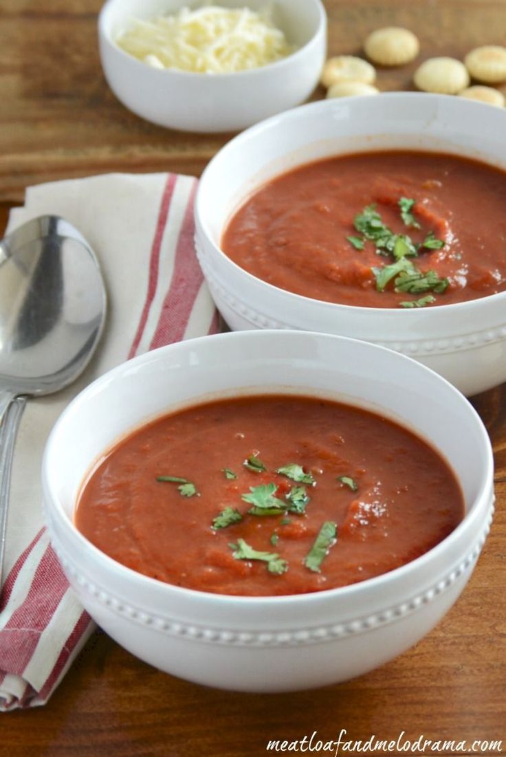 two white bowls filled with red soup and garnished with parsley on top