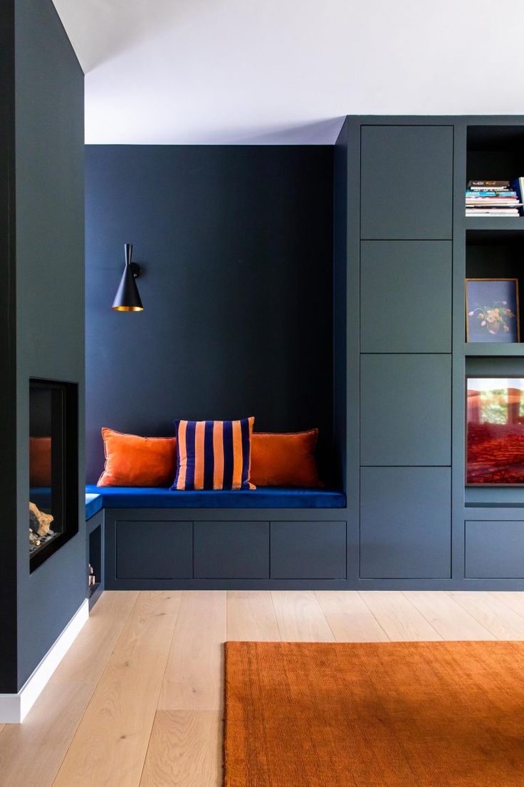 a room with blue walls and orange pillows on the bench in front of bookshelves