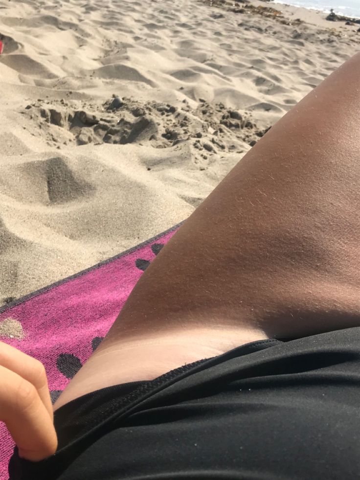 a person laying on top of a pink towel next to the ocean with their feet in the sand