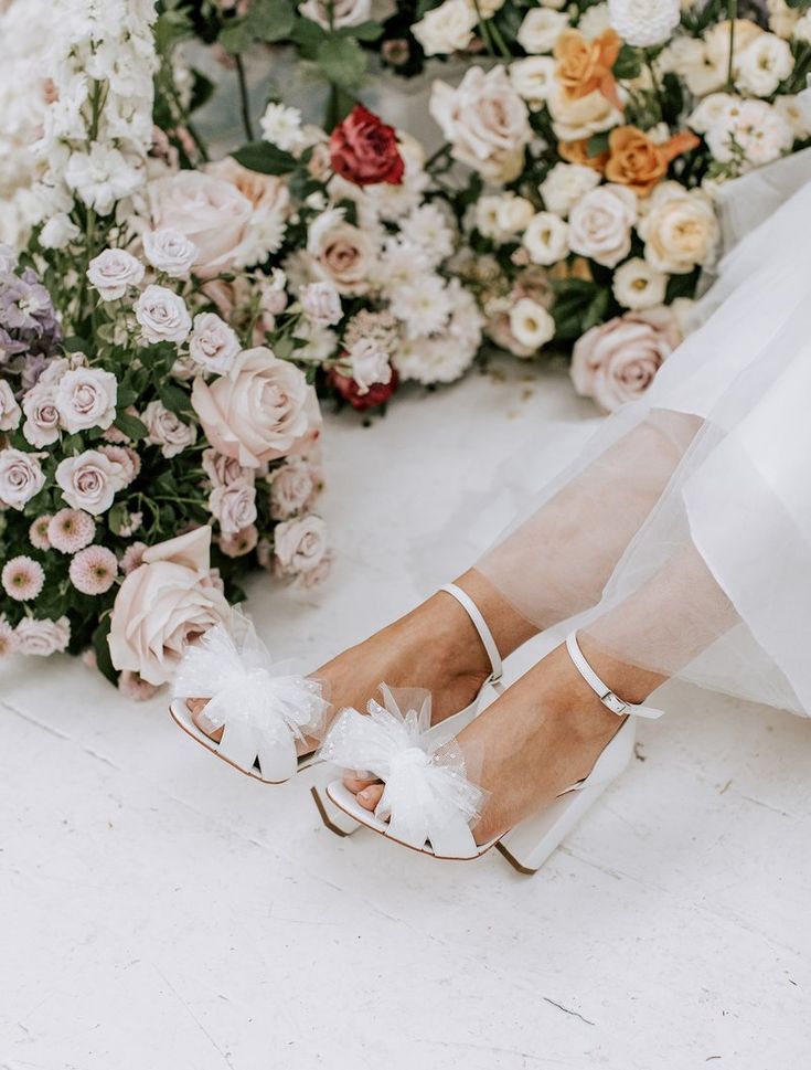 the bride's shoes are adorned with white feathers and flowers in front of them