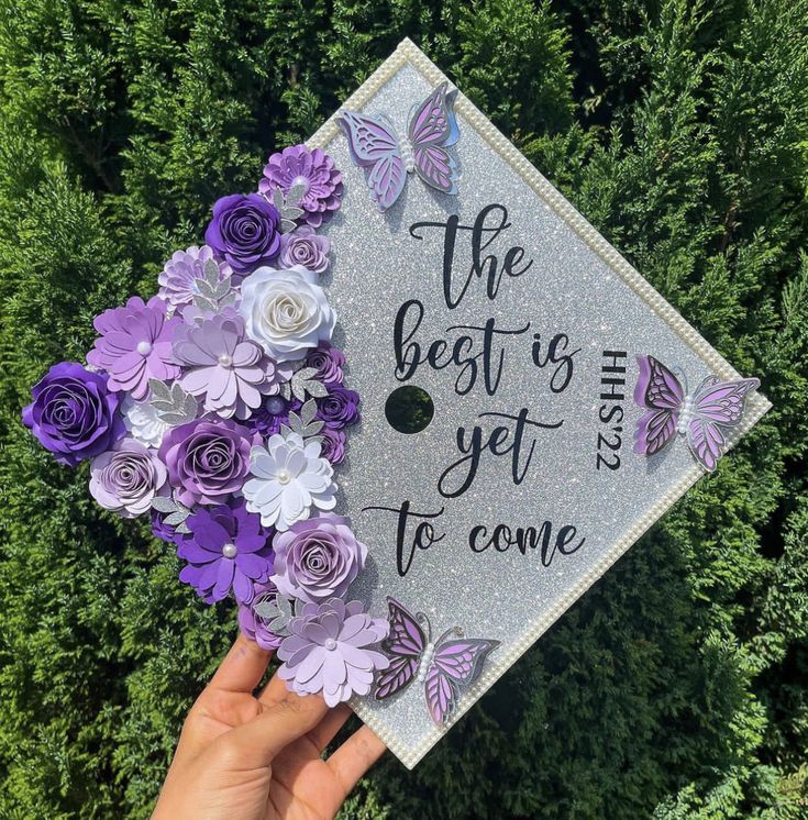 someone holding up a graduation cap with purple flowers on it that says the best is yet to come