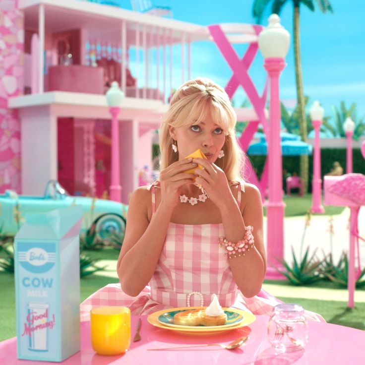 a woman sitting at a table eating food in front of a pink house with palm trees