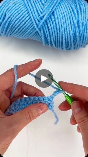 someone crocheting the ends of a blue ball of yarn with a green crochet hook