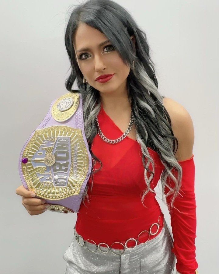 a woman in red shirt holding up a purple and gold wrestling belt