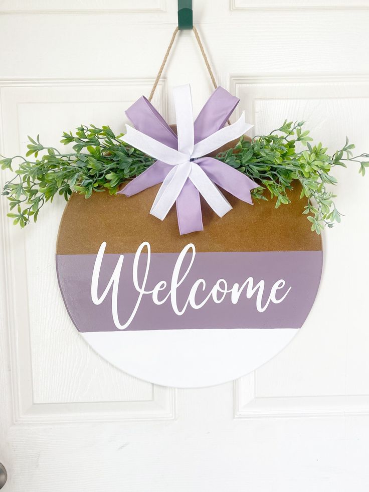 a welcome sign hanging on a door with purple and white ribbon tied around the front