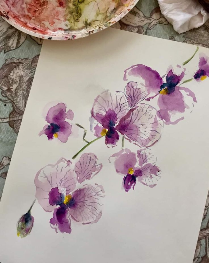 an artistically painted piece of paper with purple flowers on it next to a bowl