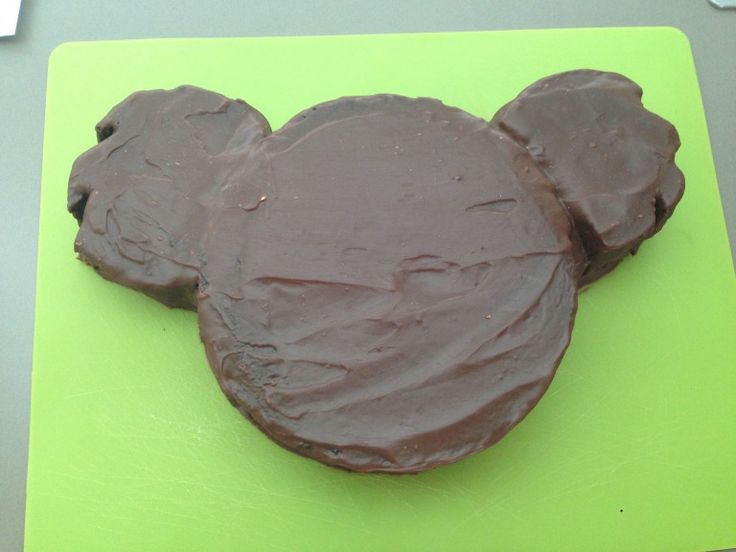 a mickey mouse shaped chocolate cake sitting on top of a green cutting board