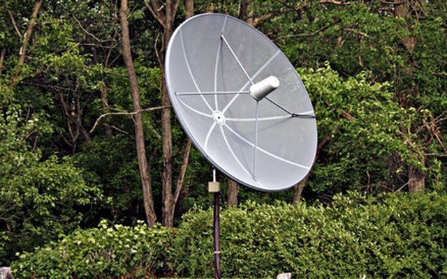 a large satellite dish sitting in the middle of a park next to some bushes and trees