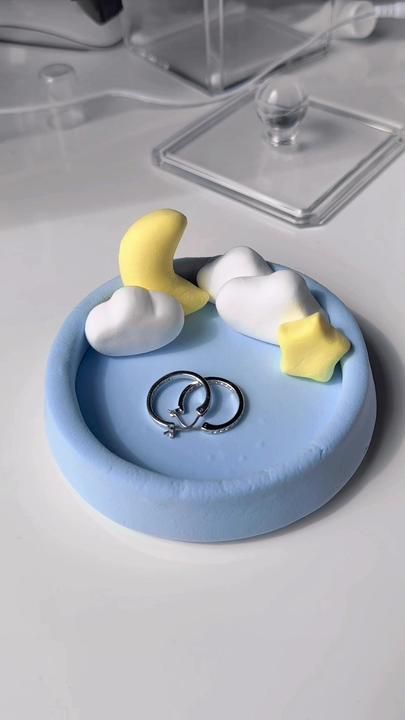 two wedding rings sitting on top of a blue and white ring holder with clouds, stars and moon